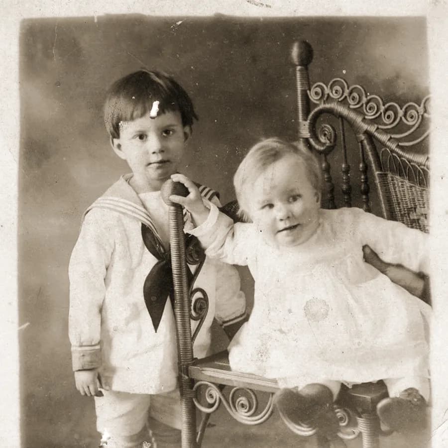 Duas crianças posando para um retrato antigo, uma delas em traje de marinheiro